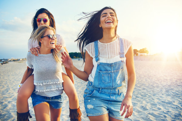 Three beautiful female friends having fun while carrying each other on beach at sunset